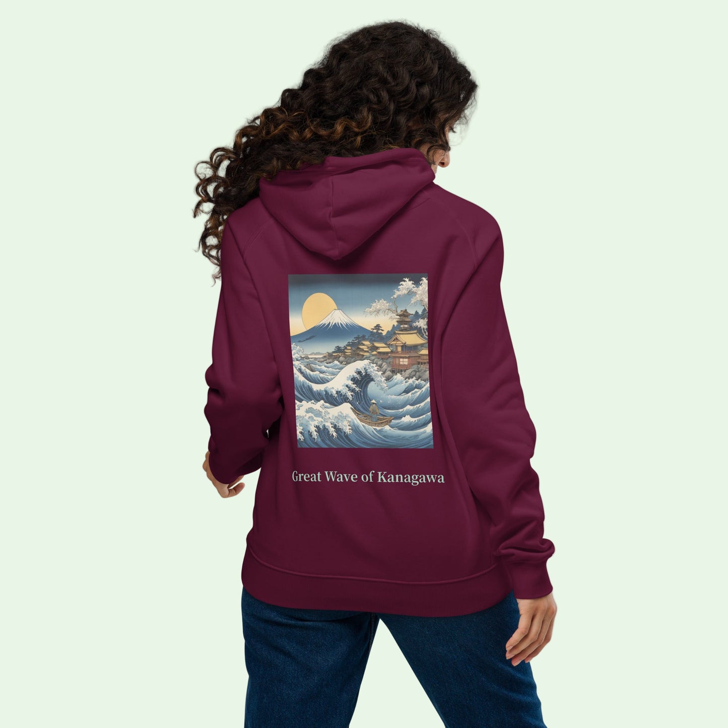 A woman wearing an unisex eco ranglan hoodie in burgundy with a Great  japanese wave back design by Aunti 